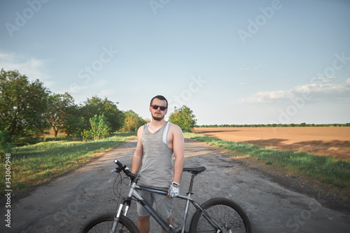 young cyclist man stands with his mountain bike and looking in to the camera. young man traveller stand on the road with his bicycle