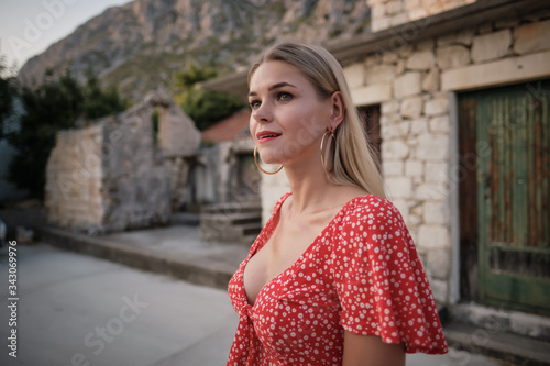 Vogue style elegant portrait of beautiful fashion woman wavy shine blonde long hair. Model in red dress with bright makeup in old town medieval Italy