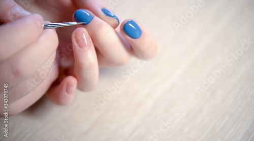 Young woman applying nail polish with brush from bottle  polishing painting fingernails with blue color enamel  doing manicure at home  perfect healthy nails care. close up view