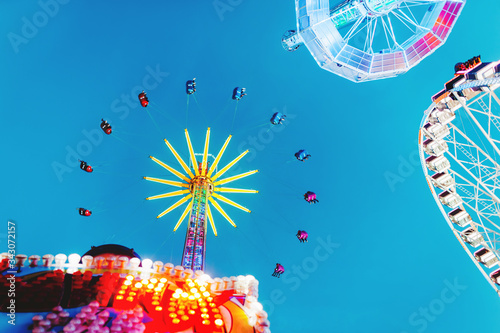 Attractionsl with neon light in amusement park with blue sky on background. Family leisure and fun on the weekend