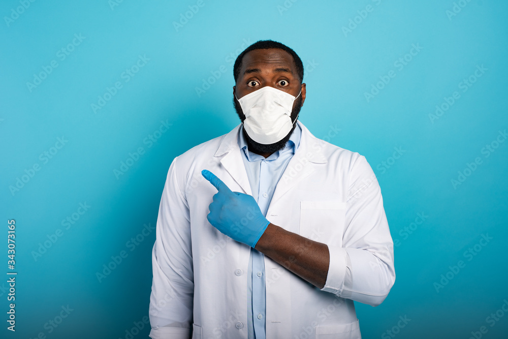 Worried medic with mask indicates something with hand. Blue background Worried medic with mask indicates something with hand. Blue background