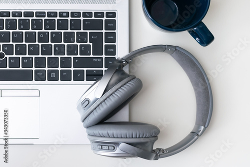 Headphones over an open laptop on a white desk and a cup on the top right side. Top point of view