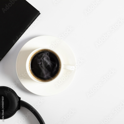 White office desk. Notebook  black headphones and coffee cup on white background.  Flat lay  top view  copy space