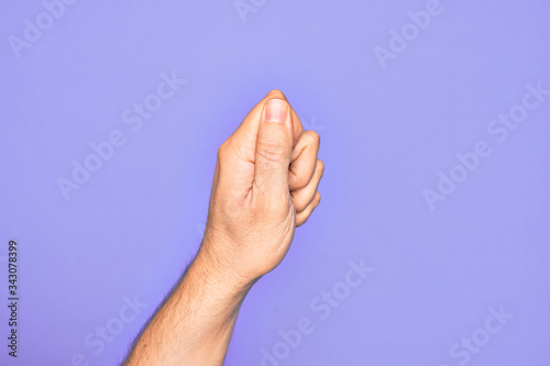 Hand of caucasian young man showing fingers over isolated purple background holding blank space with thumb finger, business and advertising