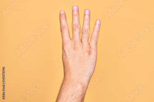 Hand of caucasian young man showing fingers over isolated yellow background counting number 4 showing four fingers