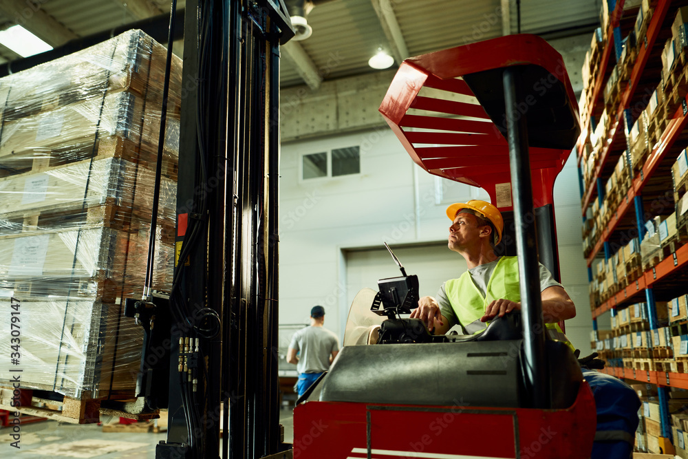 Forklift operator loading cargo while working in a warehouse.
