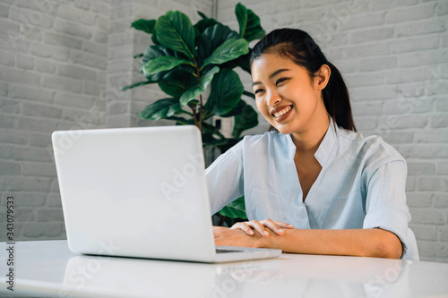 Happy friendly Asian woman using a laptop and talking, making video call conference, online job interview at home. Millennial female internet teacher tutor and vlogger working from home on the job.