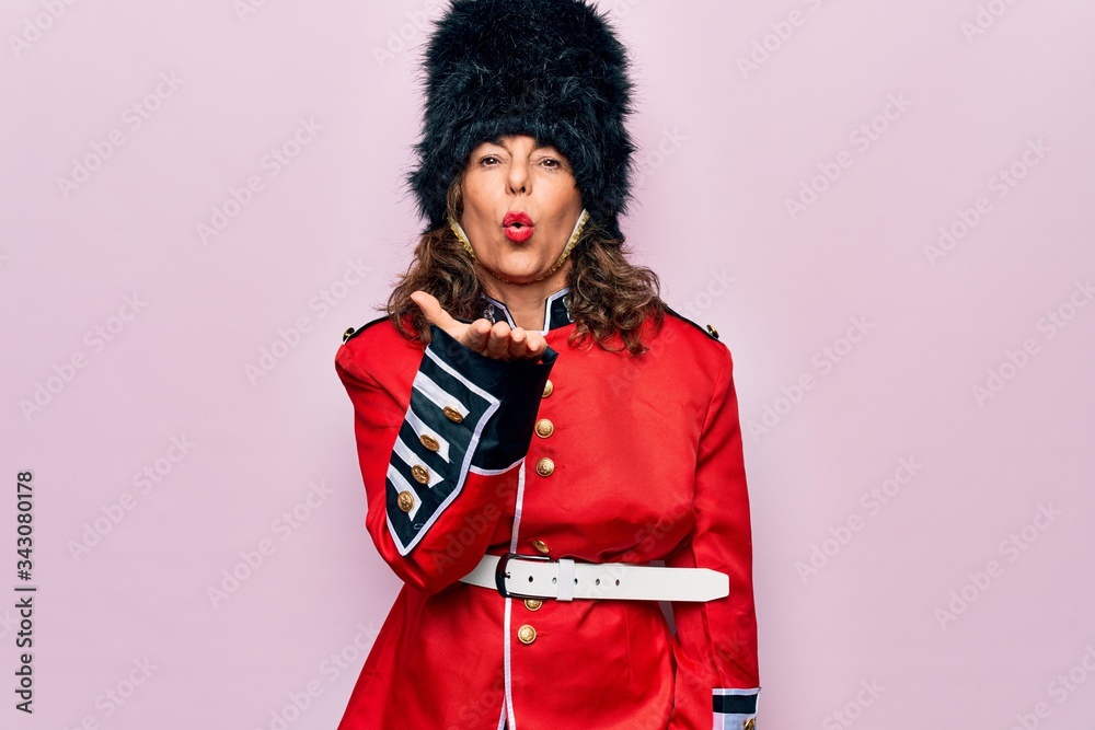 Middle age beautiful wales guard woman wearing traditional uniform over pink background looking at the camera blowing a kiss with hand on air being lovely and sexy. Love expression.