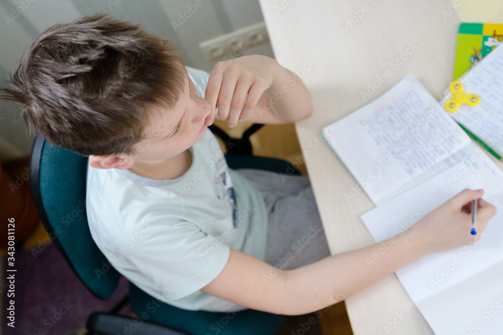 A teenager boy sits at a table in his room, doing homework. A teenager boy sits at a table in his room, doing homework.