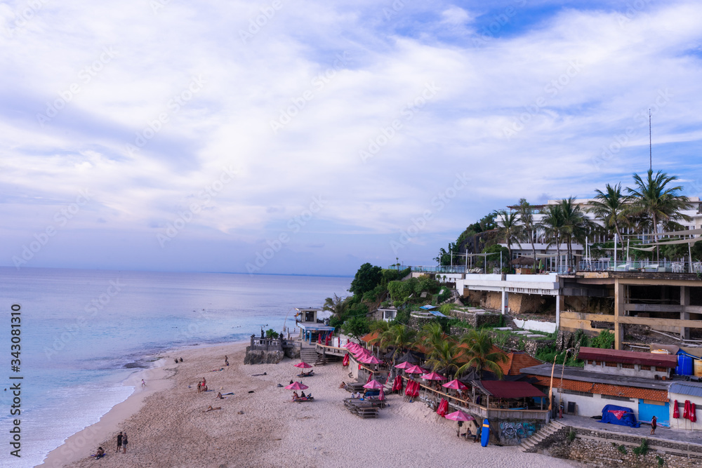 Obraz premium Beautiful deserted beach on the island of Bali at sunset. Rocks and nature. Plants and houses on the coast. Tropical paradise. Stones and white sand on the ocean