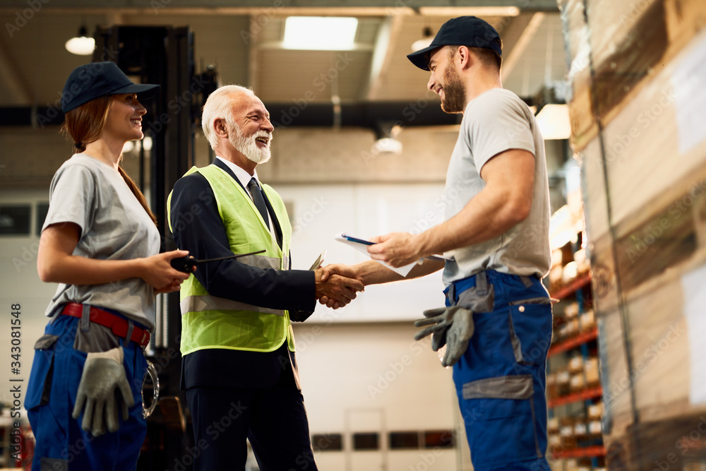 Below view of happy mature businessman shaking hands with a warehouse worker. Below view of happy mature businessman shaking hands with a warehouse worker.