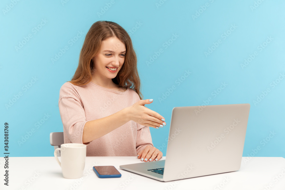 Online consulting. Happy businesswoman welcoming client with handshake and looking at laptop screen, talking on video call, conference from home office. indoor studio shot isolated on blue background Online consulting. Happy businesswoman welcoming client with handshake and looking at laptop screen, talking on video call, conference from home office. indoor studio shot isolated on blue background
