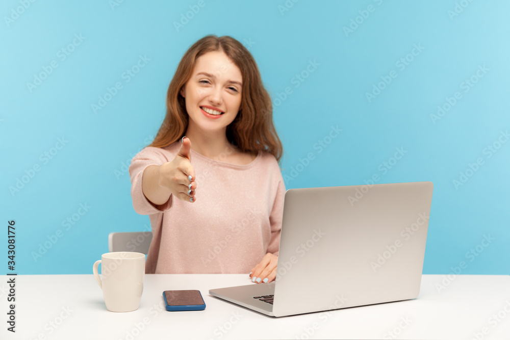Nice to meet you! Positive businesswoman with charming toothy smile giving hand to handshake, welcoming partner while working on laptop from home office. indoor studio shot isolated on blue background Nice to meet you! Positive businesswoman with charming toothy smile giving hand to handshake, welcoming partner while working on laptop from home office. indoor studio shot isolated on blue background