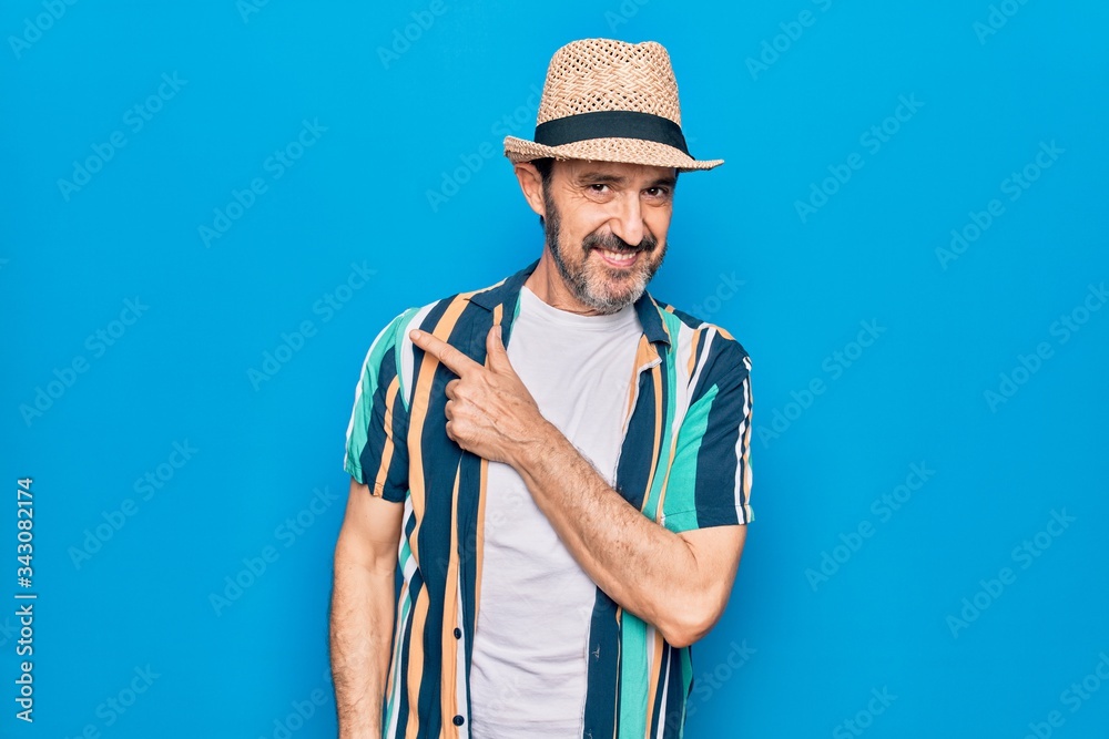 Middle age handsome tourist man on vacation wearing shirt and hat over blue background smiling cheerful pointing with hand and finger up to the side Middle age handsome tourist man on vacation wearing shirt and hat over blue background smiling cheerful pointing with hand and finger up to the side