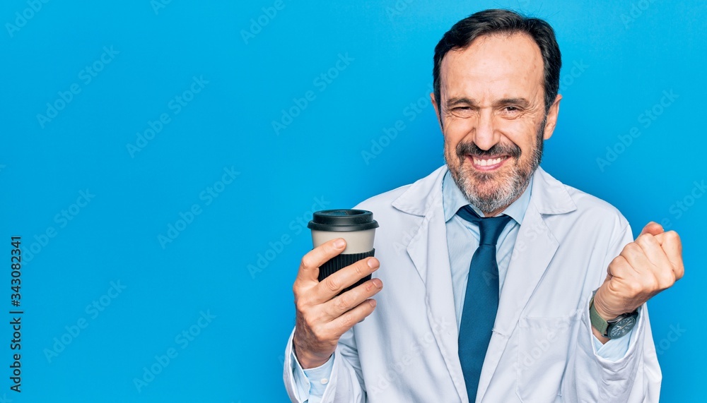 Middle age handsome doctor man wearing coat drinking cup of takeaway coffee screaming proud, celebrating victory and success very excited with raised arm Middle age handsome doctor man wearing coat drinking cup of takeaway coffee screaming proud, celebrating victory and success very excited with raised arm