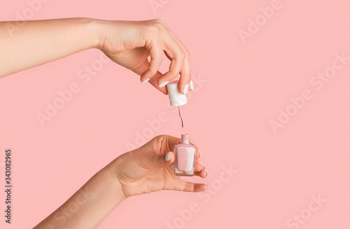 Unrecognizable nail tech opening bottle of polish on pink background, closeup. Empty space