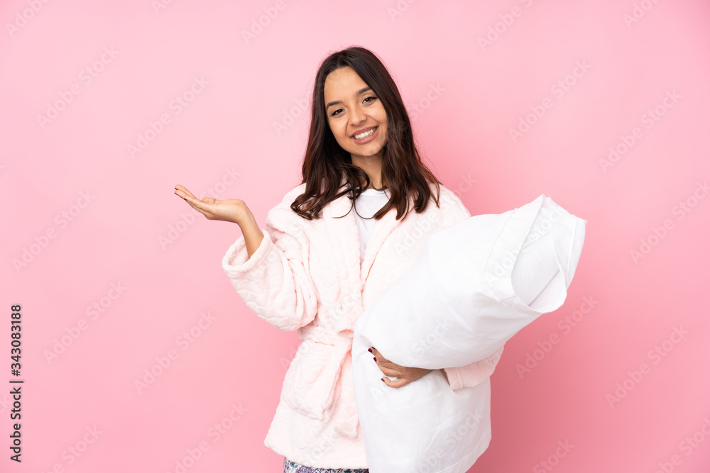 Young woman in pajamas isolated on pink background holding copyspace imaginary on the palm to insert an ad Young woman in pajamas isolated on pink background holding copyspace imaginary on the palm to insert an ad