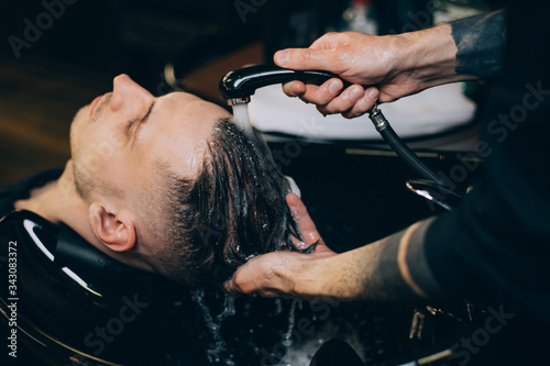 Profile view of bearded man getting his hair washed and his head massaged in hair salon. Cleaning head barber's. Barber men washing client's hair in barbershop or beaty salon © Иван Шенец