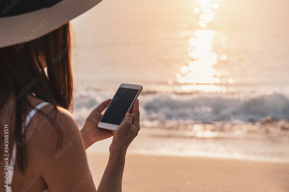 Young woman traveler using mobile phone on tropical beach at sunset, vacation and summer concept Young woman traveler using mobile phone on tropical beach at sunset, vacation and summer concept