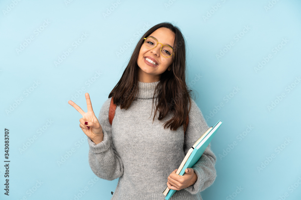 Young mixed race woman going to school isolated on blue background showing victory sign with both hands Young mixed race woman going to school isolated on blue background showing victory sign with both hands