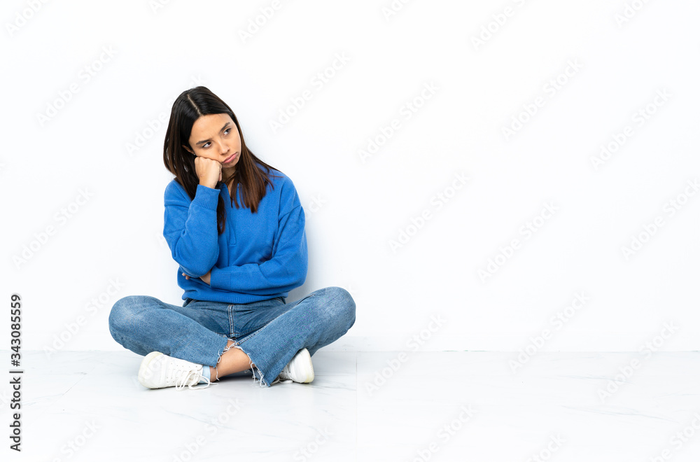 Young mixed race woman sitting on the floor isolated on white background whispering something with surprise gesture while looking to the side Young mixed race woman sitting on the floor isolated on white background whispering something with surprise gesture while looking to the side