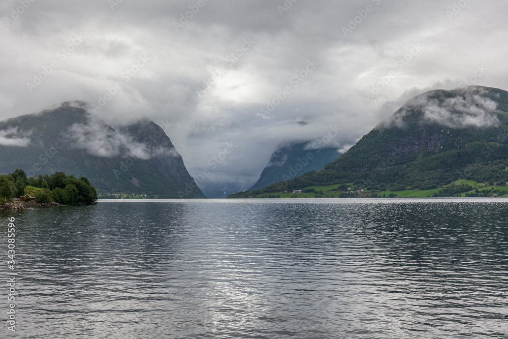 Norwegian fjord and mountains surrounded by clouds, ideal fjord reflection in clear water. selective focus.