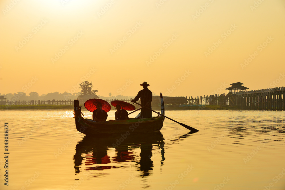 monk in boat at U-Bein bridge on during sunrise, Mandalay Myanmar