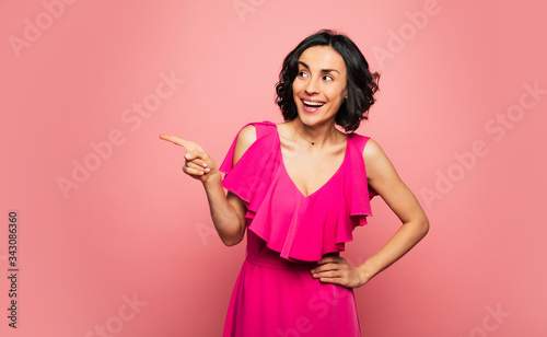 Pink dress. Close-up photo of attractive girl in a pink dress, who is looking and pointing to the left, while laughing joyfully. © My Ocean studio