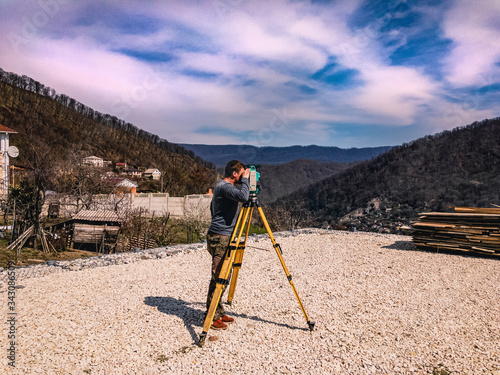 Surveyor with a total station at work. A set of a total station and a surveyor taking measurements at a construction site against the backdrop of the mountains. Construction work on a sunny day.