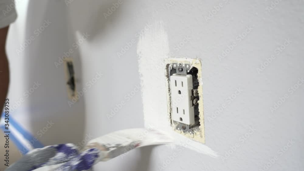Close up of painter hands with gloves painting the wall around power outlet.