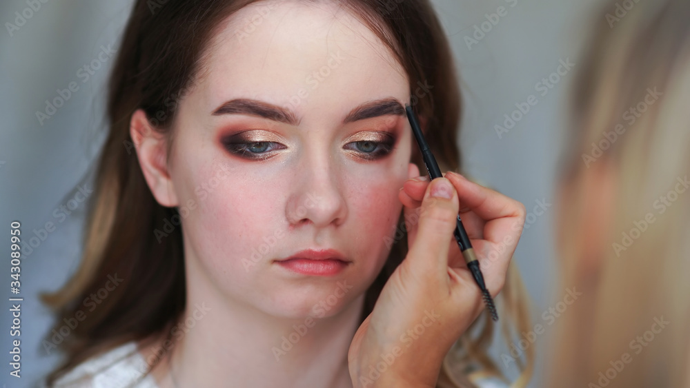 Makeup artist paints eyebrows of a young girl. Makeup artist paints eyebrows of a young girl.