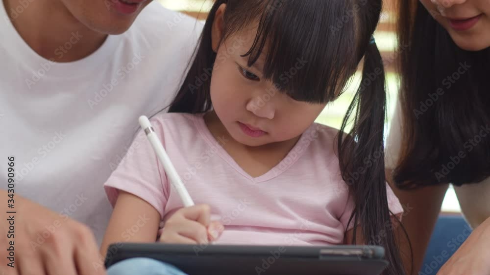 Happy Asian family dad, mom and daughter using computer tablet technology sitting sofa in living room at house. Self-isolation, stay at home, social distancing, quarantine for coronavirus prevention. Happy Asian family dad, mom and daughter using computer tablet technology sitting sofa in living room at house. Self-isolation, stay at home, social distancing, quarantine for coronavirus prevention.