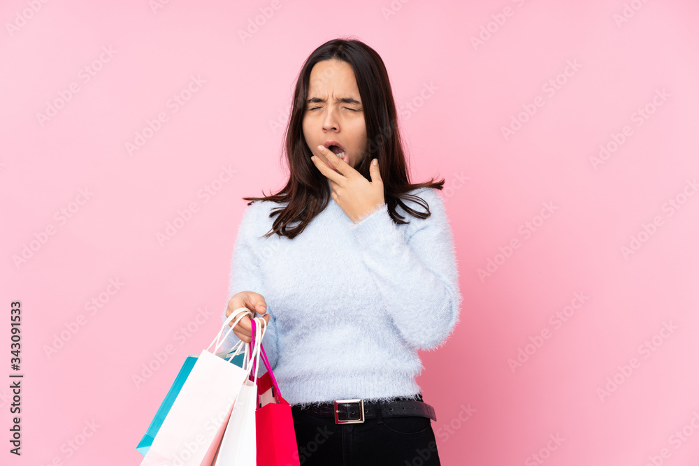 Young woman with shopping bag over isolated pink background yawning