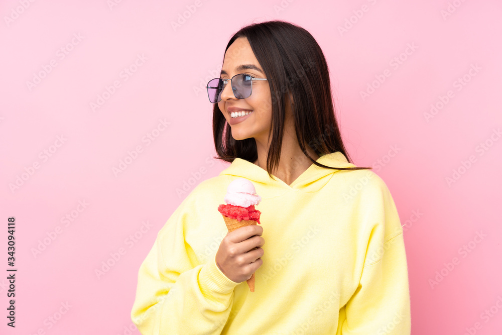 Young brunette girl holding a cornet ice cream over isolated pink background looking side Young brunette girl holding a cornet ice cream over isolated pink background looking side