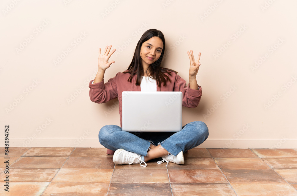 Young mixed race woman with a laptop sitting on the floor counting eight with fingers Young mixed race woman with a laptop sitting on the floor counting eight with fingers