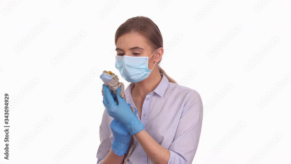 Young lady holding her pet bearded agama lizard wearing sterile medical mask, funny COVID-19 quarantine concept Young lady holding her pet bearded agama lizard wearing sterile medical mask, funny COVID-19 quarantine concept