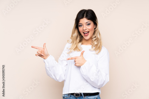Teenager girl isolated on beige background surprised and pointing side