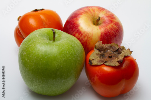 Two apples one green one red yellow and two persimmons orange on a light background