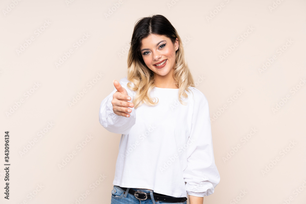 Teenager girl isolated on beige background shaking hands for closing a good deal Teenager girl isolated on beige background shaking hands for closing a good deal