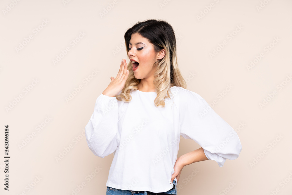 Teenager girl isolated on beige background yawning and covering wide open mouth with hand Teenager girl isolated on beige background yawning and covering wide open mouth with hand