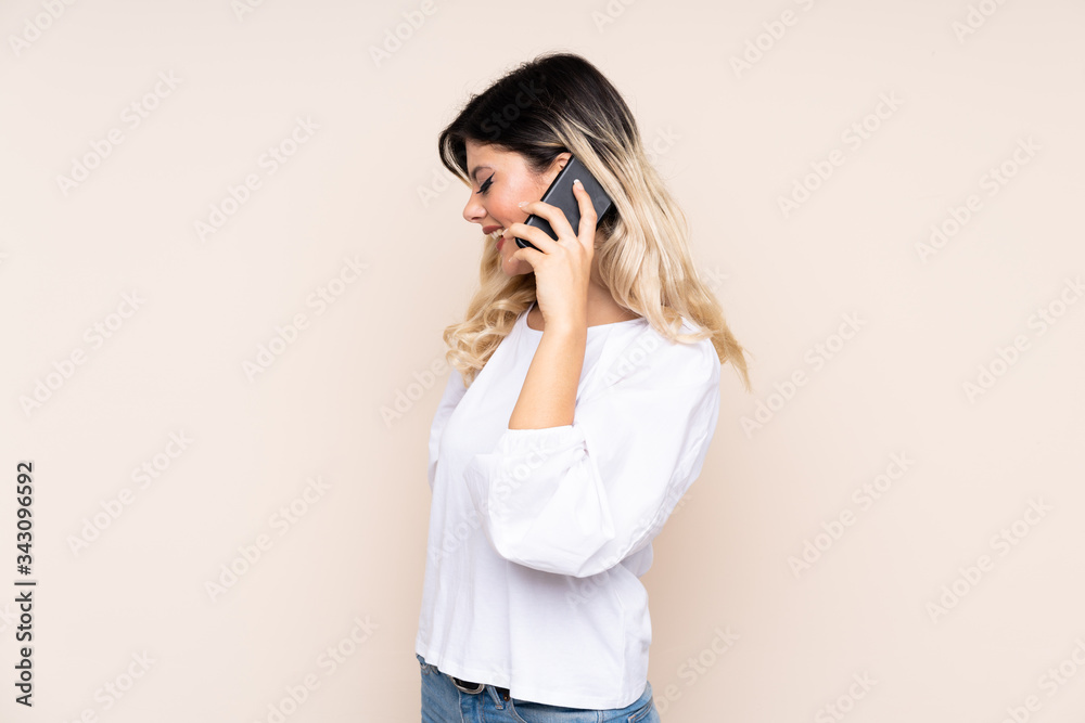 Teenager girl isolated on beige background keeping a conversation with the mobile phone with someone Teenager girl isolated on beige background keeping a conversation with the mobile phone with someone