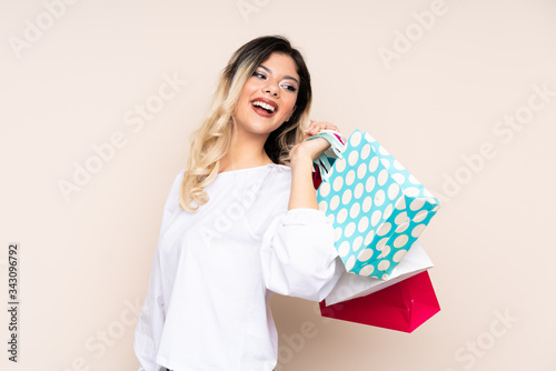 Teenager girl isolated on beige background holding shopping bags and smiling