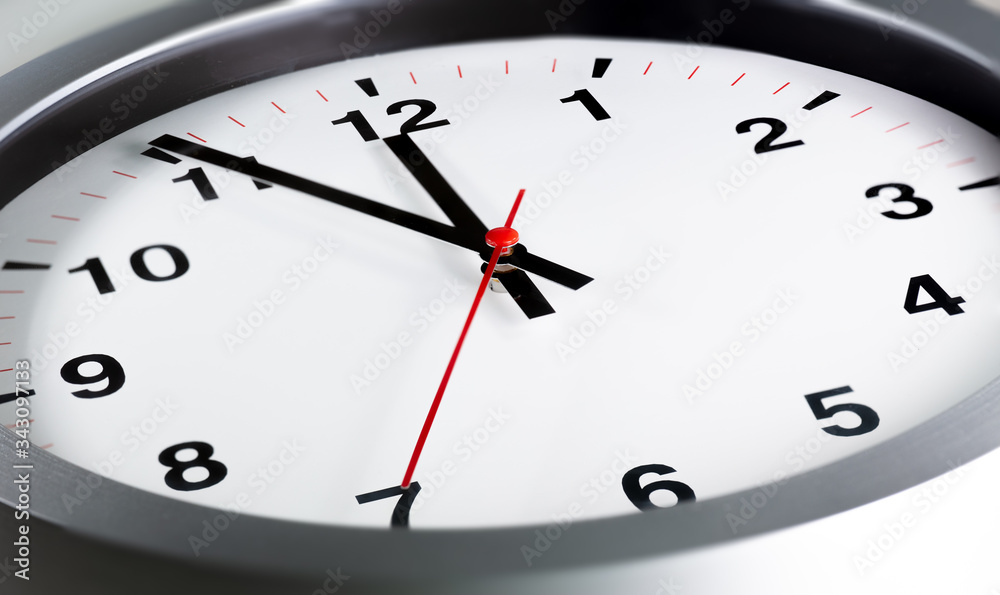 It is five to twelve, the clock is ticking. Modern white grey clock shows the time 5 before 12. Close up to a wall clock, with five minutes to twelve o'clock. Time is running out It is five to twelve, the clock is ticking. Modern white grey clock shows the time 5 before 12. Close up to a wall clock, with five minutes to twelve o'clock. Time is running out