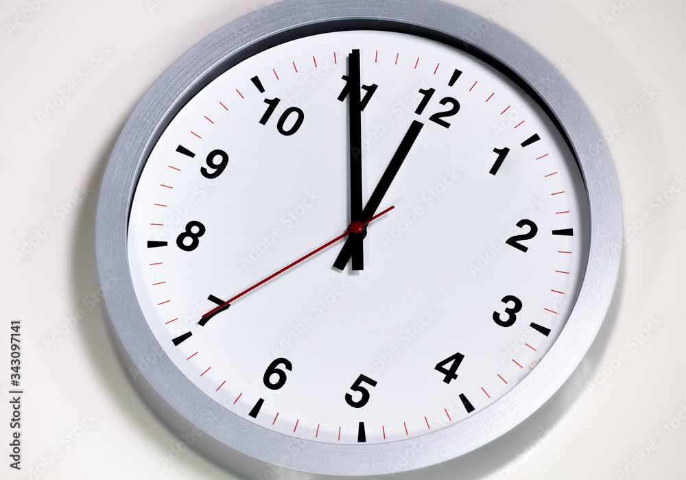 It is five to twelve, the clock is ticking. Modern white grey clock shows the time 5 before 12. Close up to a wall clock, with five minutes to twelve o'clock. Time is running out It is five to twelve, the clock is ticking. Modern white grey clock shows the time 5 before 12. Close up to a wall clock, with five minutes to twelve o'clock. Time is running out