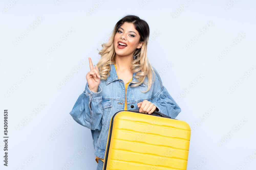 Traveler teenager holding a suitcase isolated on blue background in vacation with travel suitcase Traveler teenager holding a suitcase isolated on blue background in vacation with travel suitcase