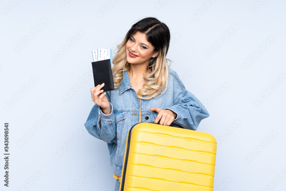 Traveler teenager holding a suitcase isolated on blue background in vacation with suitcase and passport Traveler teenager holding a suitcase isolated on blue background in vacation with suitcase and passport