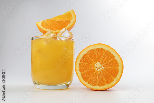 Fresh yellow orange juice in glass with orange slice and ice cube on white background