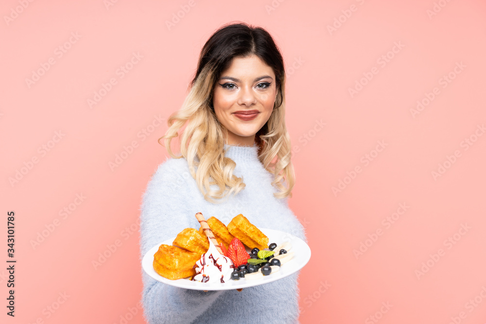 Teenager girl holding waffles on isolated pink background with happy expression Teenager girl holding waffles on isolated pink background with happy expression