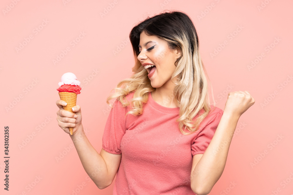Teenager girl holding a cornet ice cream isolated on pink background celebrating a victory Teenager girl holding a cornet ice cream isolated on pink background celebrating a victory