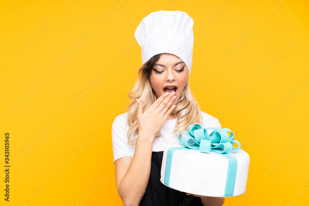 Teenager girl pastry holding a big cake isolated on yellow background Teenager girl pastry holding a big cake isolated on yellow background